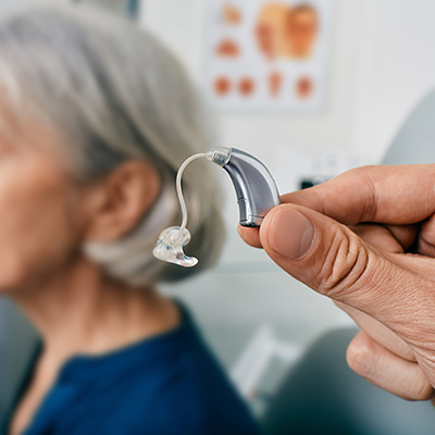 Audiologist holding an hearing aid with patient in the background. 